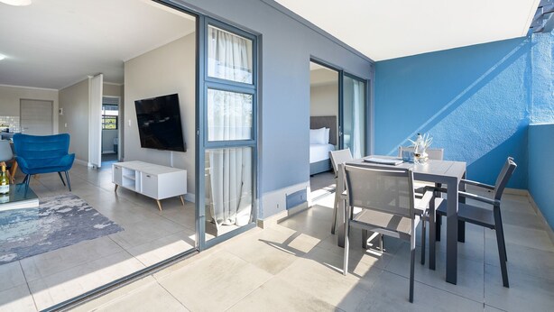 A modern living space with a dining area, a TV mounted on the wall, and a large sliding glass door leading to an outdoor area. - The Terraces 220 (Cape Town)