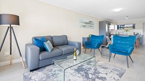 A modern living room with a grey sofa, two blue armchairs, a glass coffee table, and a floor lamp. - The Terraces 220 (Cape Town)