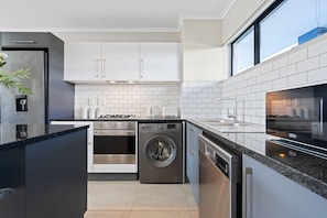 Eine moderne Küche mit weißen Schränken, einem Edelstahlkühlschrank, einem eingebauten Backofen, einem Geschirrspüler und einem Fenster über der Spüle.
