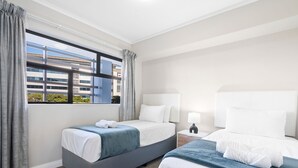A hotel room with two beds, a window with curtains, a nightstand with a lamp, and a view of a building outside. - The Terraces 220 (Cape Town)