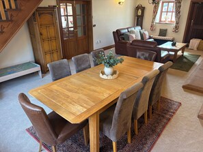 A dining area with a wooden table, grey upholstered chairs, and a vase with greenery. - The Shippon (Ormskirk)