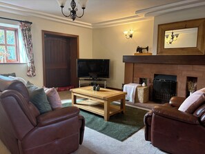 A living room with leather sofas, a wooden coffee table, a television, a fireplace, and a door. - The Shippon (Ormskirk)