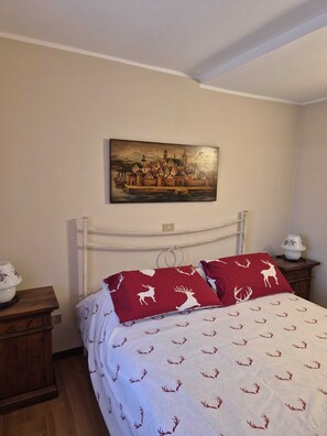 A bedroom with a bed, a nightstand, a lamp, a painting on the wall, and a patterned bedspread. - House with garden and garage near the slopes (San Pietro)