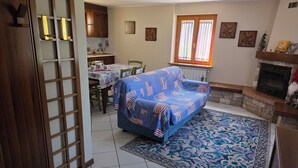 A living room with a sofa, dining table, chairs, a fireplace, and a window with curtains. - House with garden and garage near the slopes (San Pietro)