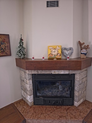 A fireplace with a stone surround, a small Christmas tree, and a clock on the mantel. - House with garden and garage near the slopes (San Pietro)