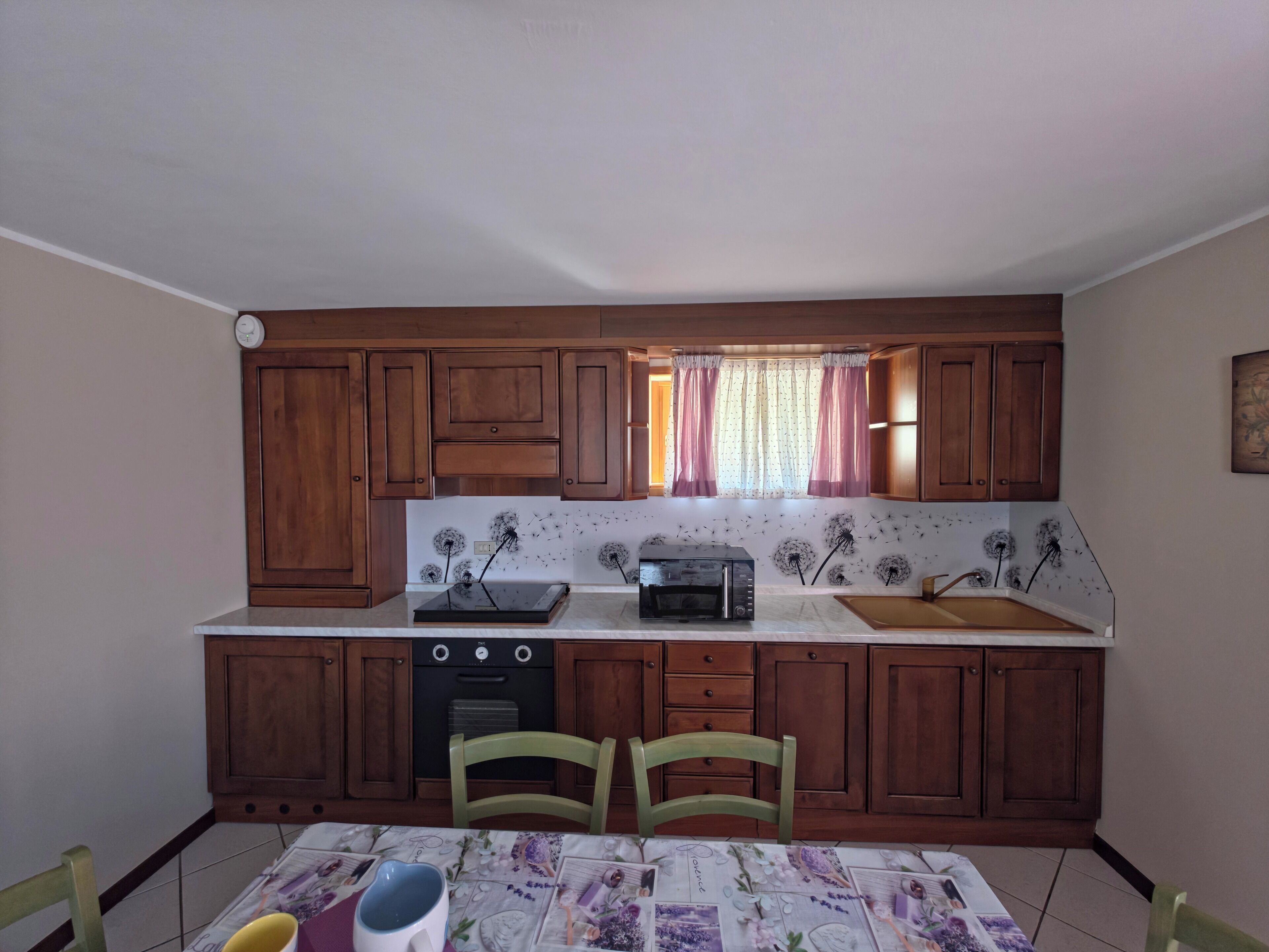 A compact kitchen with wooden cabinets, a microwave, a toaster, and a window with curtains.