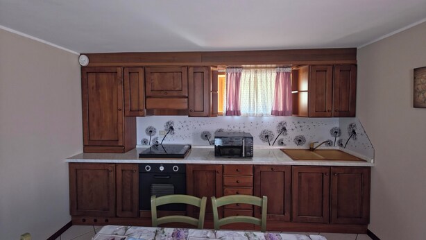 A compact kitchen with wooden cabinets, a microwave, a toaster, and a window with curtains. - House with garden and garage near the slopes (San Pietro)