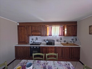 A compact kitchen with wooden cabinets, a microwave, a toaster, and a window with curtains. - House with garden and garage near the slopes (San Pietro)