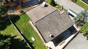 An aerial view of a residential building with a sloped roof, a fenced yard, and a street visible in the background. - House with garden and garage near the slopes (San Pietro)