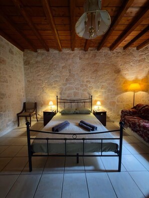 A bedroom with a metal bed frame, two bedside lamps, a chair, and a stone wall. - A stone retreat 40m from the sea, in a private 1,200m² estate on Aegina island. (Aegina)