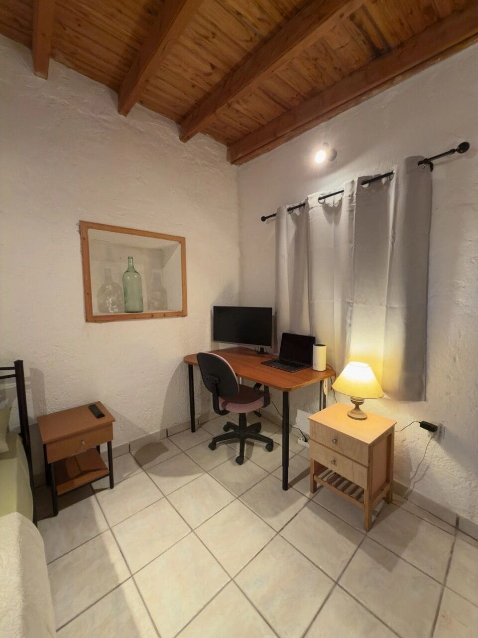 Ein Zimmer mit Holzboden, einem Schreibtisch mit Computer, einem Stuhl, einer Lampe und einem kleinen Tisch.