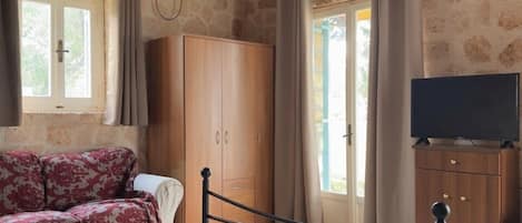 Une chambre à coucher avec un lit, une armoire, une télévision et un mur en pierre.