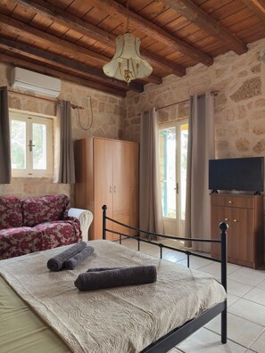 A bedroom with a bed, a wardrobe, a television, and a stone wall. - A stone retreat 40m from the sea, in a private 1,200m² estate on Aegina island. (Aegina)