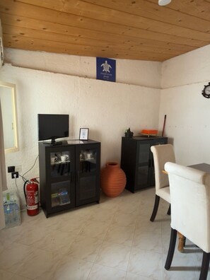 Ein Zimmer mit Fernseher auf einem Schrank, einem Sessel, einer großen Vase und einem Feuerlöscher.