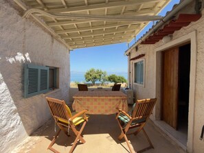 An outdoor patio with a table and chairs, a covered area, and a view of the sea. - A stone retreat 40m from the sea, in a private 1,200m² estate on Aegina island. (Aegina)