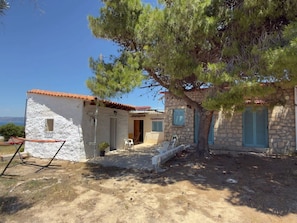 A rustic stone building with a red-tiled roof, a small porch, and a tree providing shade. - A stone retreat 40m from the sea, in a private 1,200m² estate on Aegina island. (Aegina)