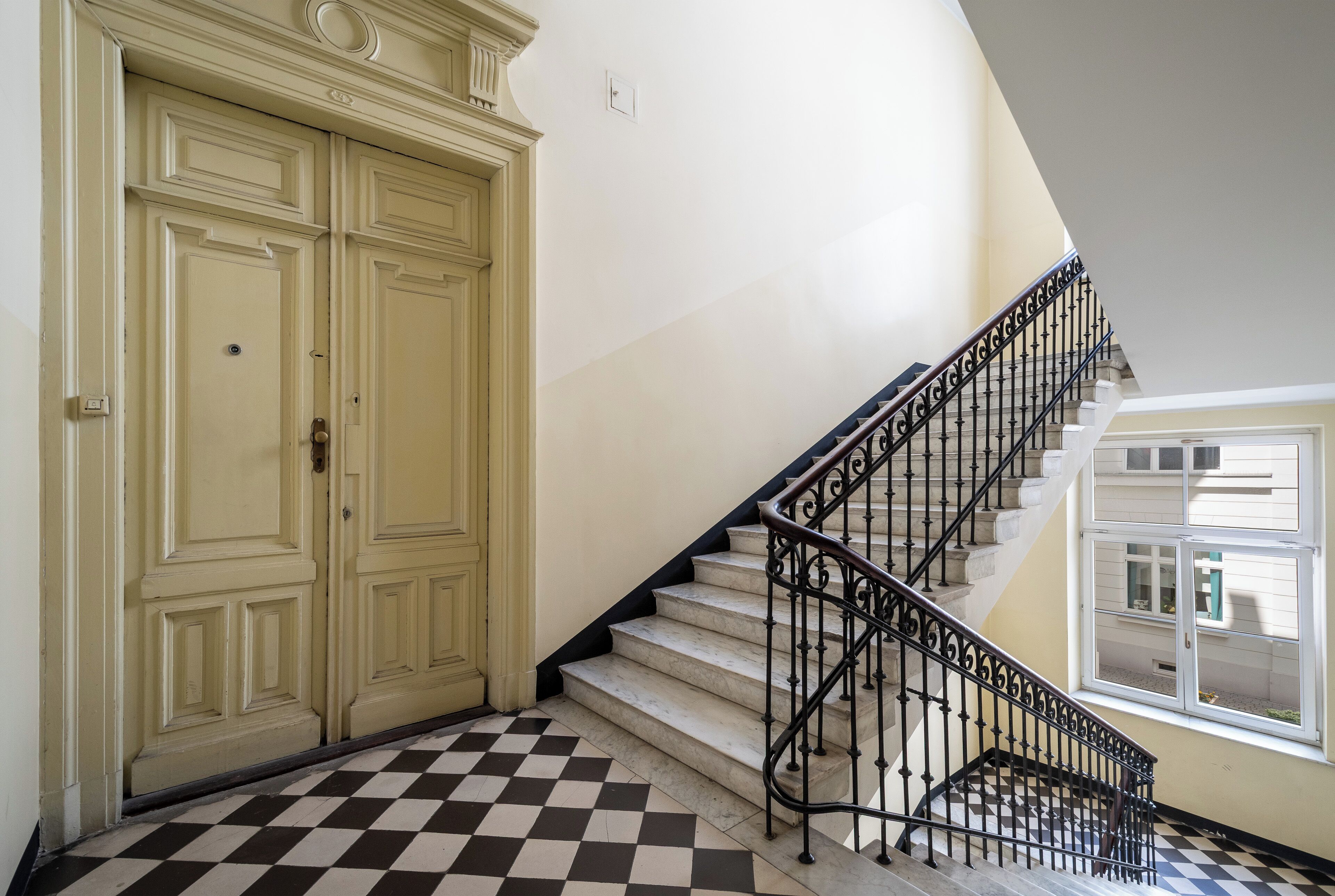 Una escalera con suelo a cuadros que conduce a un rellano con puertas dobles.