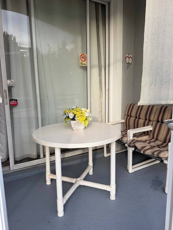 A round table with a white surface and a flower vase, a striped sofa, and a sliding glass door with a 'No Smoking' sign. - Windsor Palms apartment near Disney (Kissimmee)