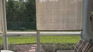 Ein Zimmer mit Blick auf eine Wiese und einen Zaun, eine Couch, ein Tisch und ein Fenster mit Fliegengitter.