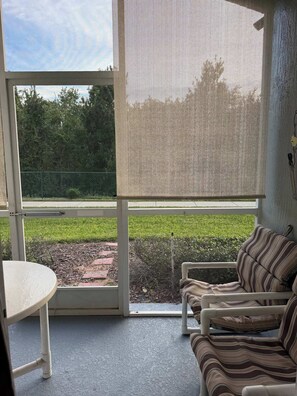 Ein Zimmer mit Blick auf eine Wiese und einen Zaun, eine Couch, ein Tisch und ein Fenster mit Fliegengitter.