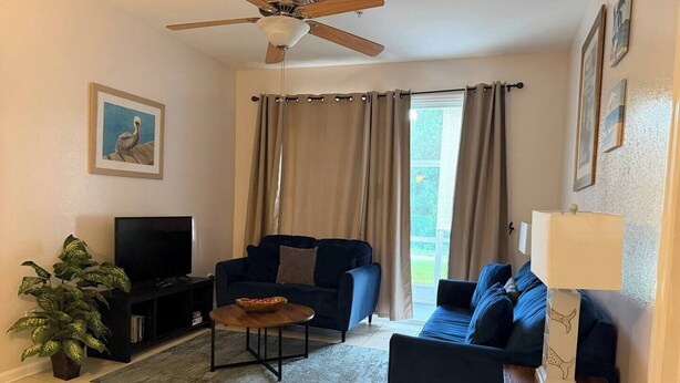 Ein Wohnzimmer mit Deckenventilator, Fernseher, Sofa, Couchtisch und Lampe.