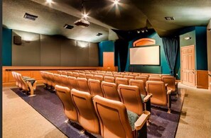 Ein Theater mit Sitzreihen, einer Leinwand und einem Projektor.