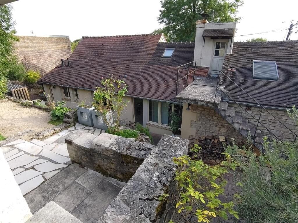 A residential property with a stone wall, a small garden, and a house with a tiled roof.