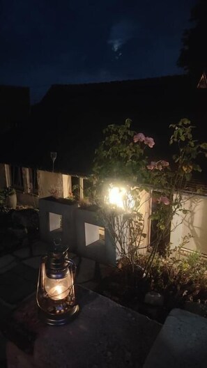 A lantern on a stone surface, a garden with plants and a wall, and a building in the background.