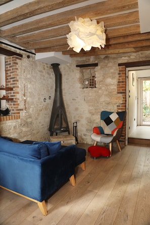 Una habitación rústica con vigas de madera a la vista, una pared de piedra, un sofá azul, una silla roja y una chimenea grande y negra.