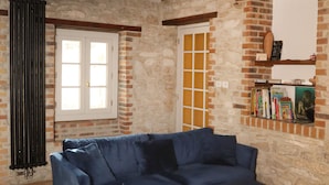 Une pièce avec un canapé d’angle bleu, un fauteuil rouge, un plancher en bois, un mur en briques et un luminaire suspendu.