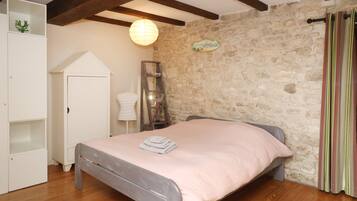A bedroom with a stone wall, a bed with a pink bedspread, a wardrobe, and a small shelf with decorative items.