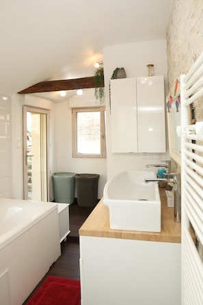 Ein Badezimmer mit einer weißen Badewanne, einem Waschbecken, einem Spiegel und einem Fenster.
