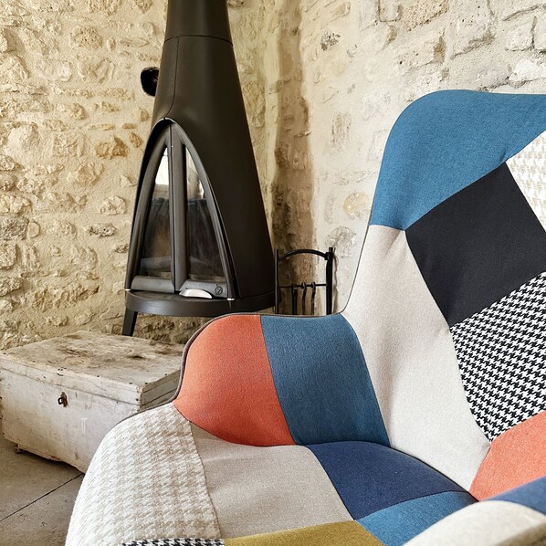 Une pièce chaleureuse avec un mur en pierre, une cheminée et un canapé coloré à motifs matelassés.