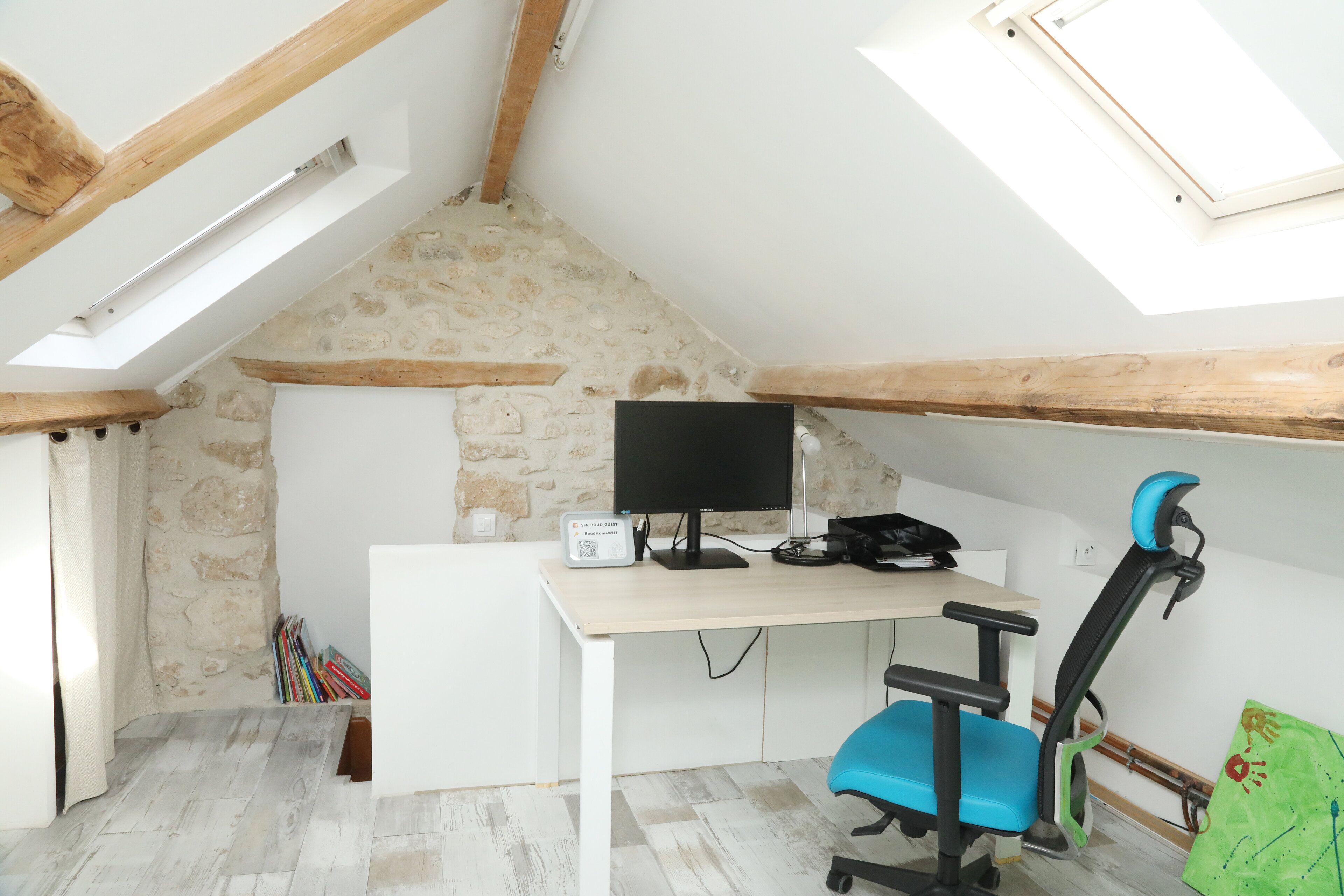 A room with a sloped ceiling, a desk with a computer, a chair, and a bookshelf.