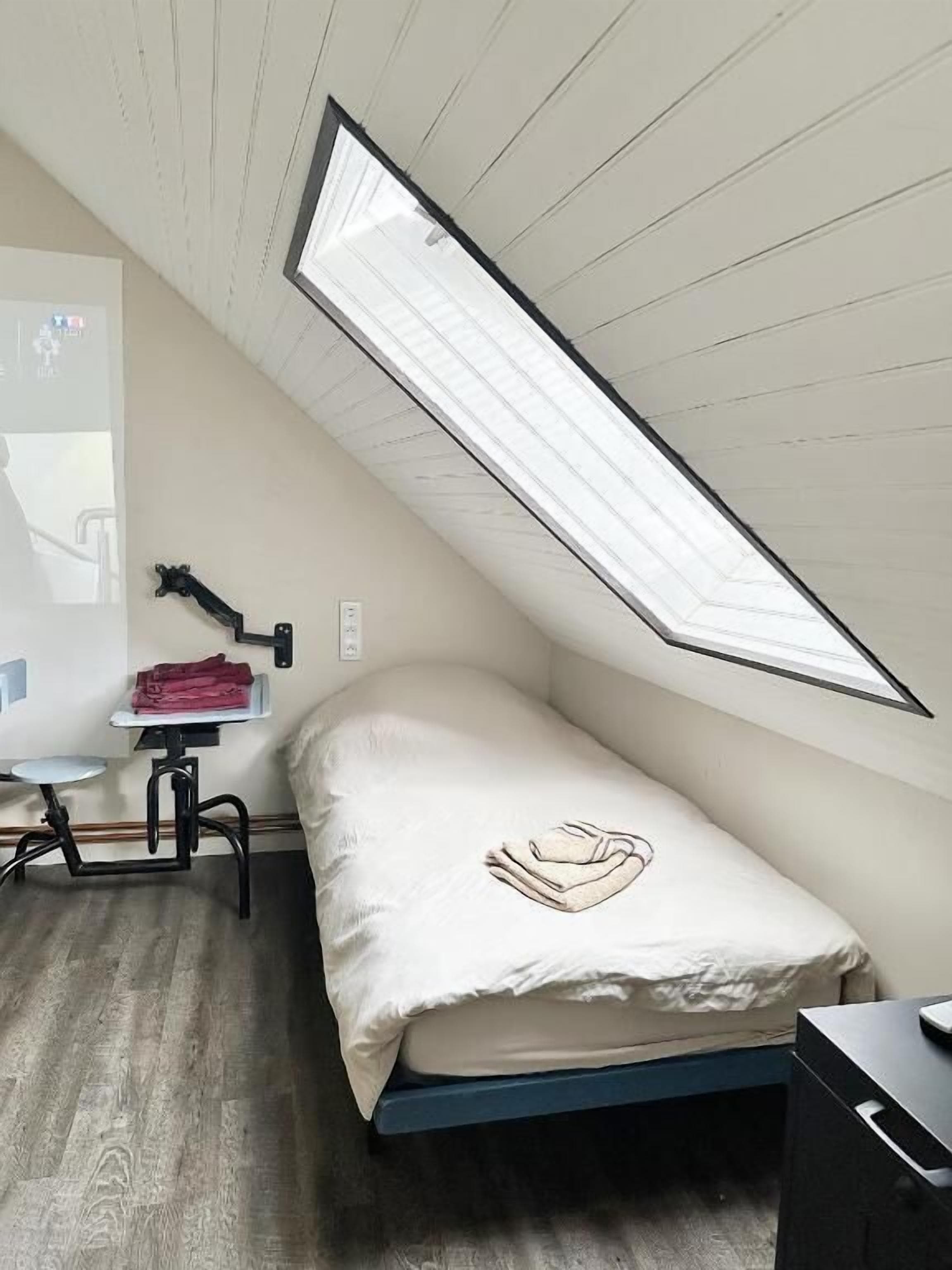 Ein kleines Zimmer mit einem Einzelbett, geneigter Decke und einem Oberlicht.