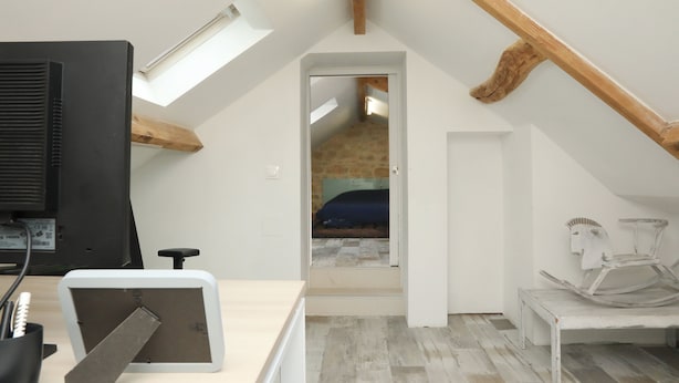 Une chambre mansardée avec un plafond en pente, un lit, un bureau avec un ordinateur et une chaise.