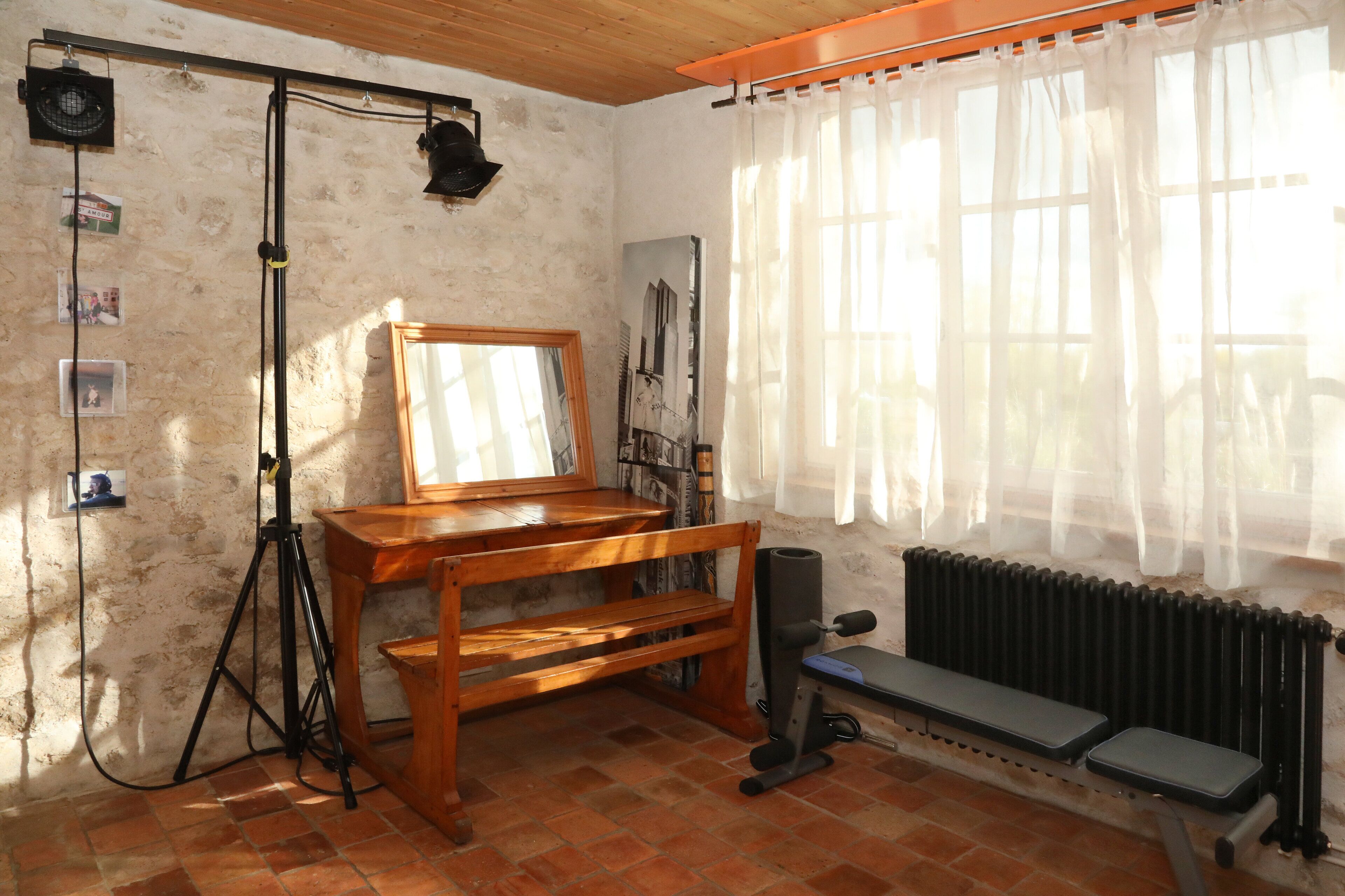 A room with a wooden desk, a mirror, a radiator, and a window with sheer curtains.