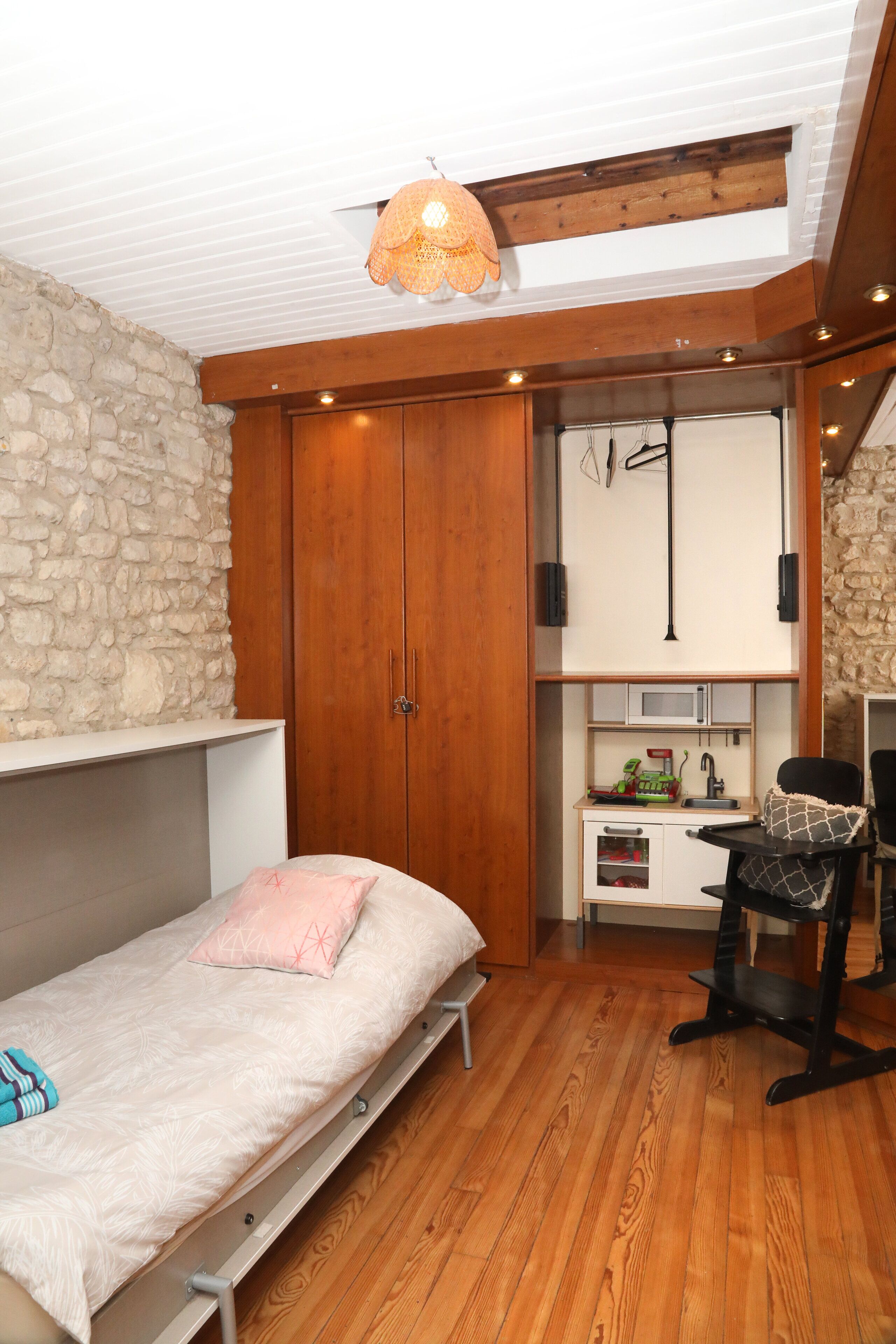 Un dormitorio con cama, escritorio, silla, armario y lámpara colgante.