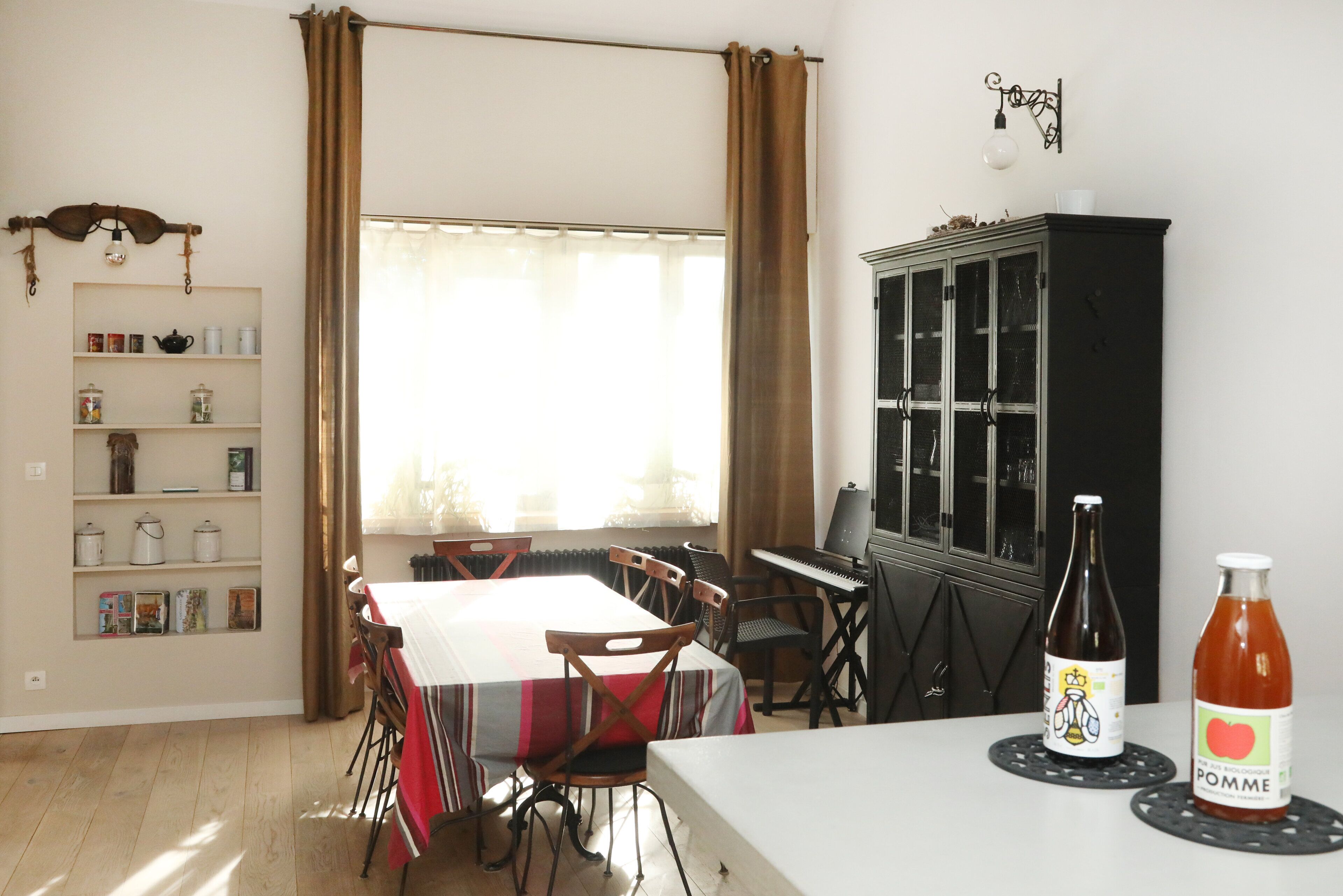 Un coin repas comprenant une table, des chaises, un piano, un buffet et une bouteille de jus de pomme.