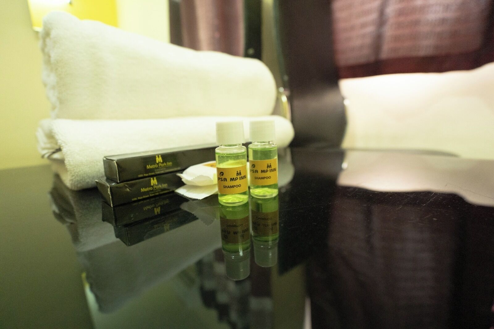 A hotel room with a black table, a Metro Park Inn branded box, and two shampoo bottles.
