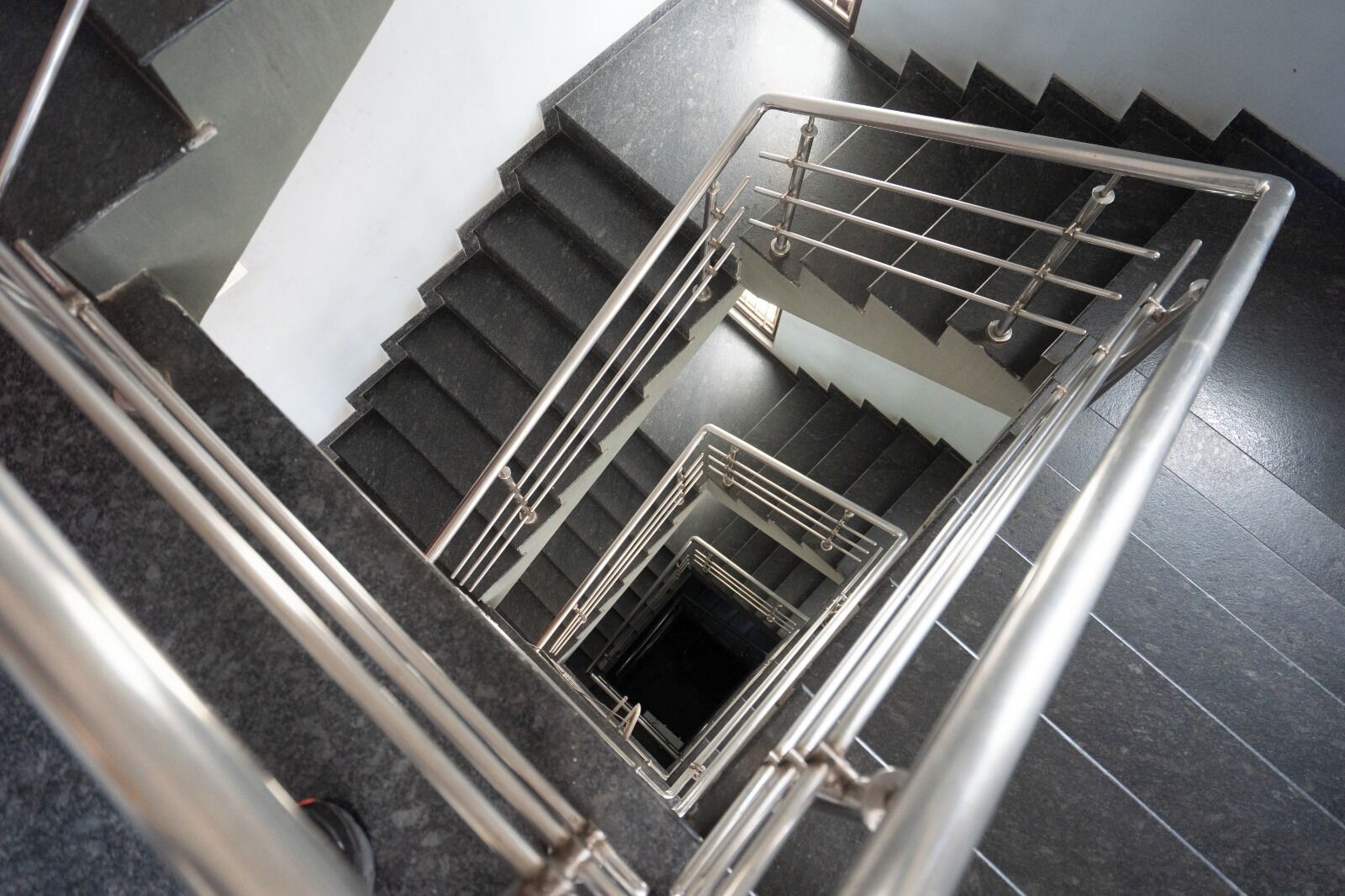Una escalera con barandilla de metal y peldaños negros.