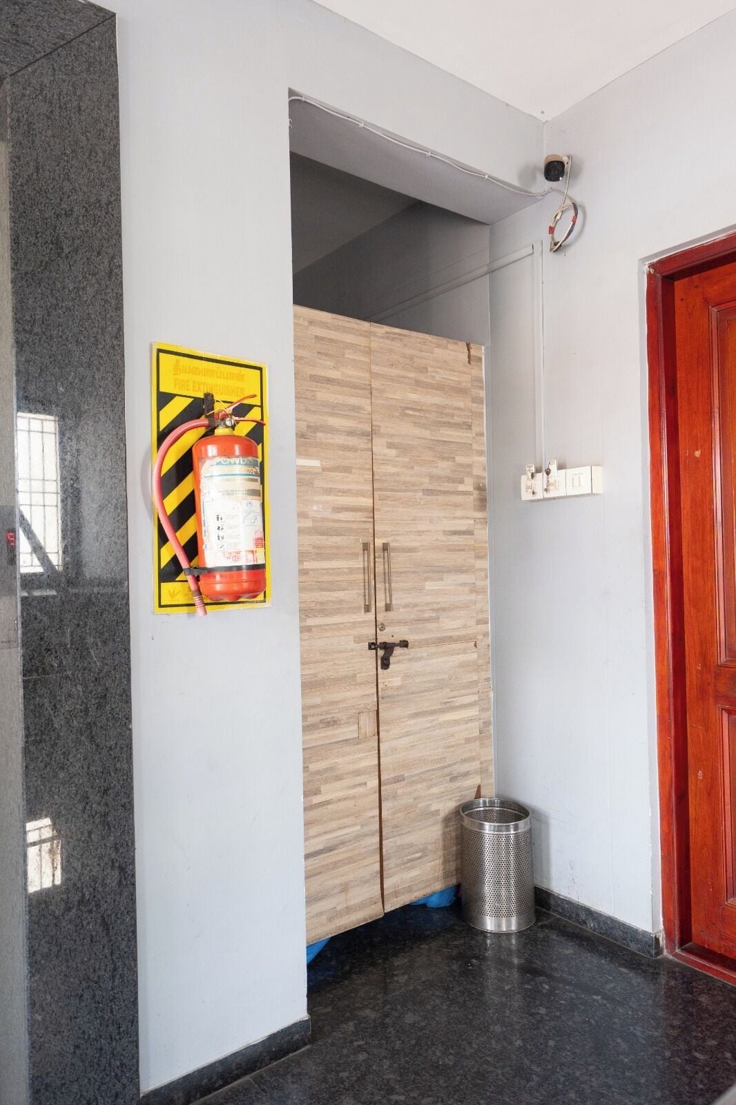 Una habitación con armario, extintor, cubo de basura y puerta.