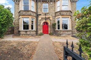A traditional stone building with a red door, multiple windows, and a brick pathway leading to the entrance. - Luxury 8 Bed House, Games Room & Free Parking (Bedford)