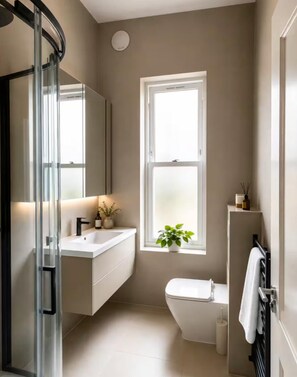 A modern bathroom with a glass shower enclosure, a white sink, a toilet, and a window with a plant. - Luxury 8 Bed House, Games Room & Free Parking (Bedford)