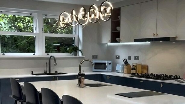 A modern kitchen with a marble island, black bar stools, and a large window. - Luxury 8 Bed House, Games Room & Free Parking (Bedford)