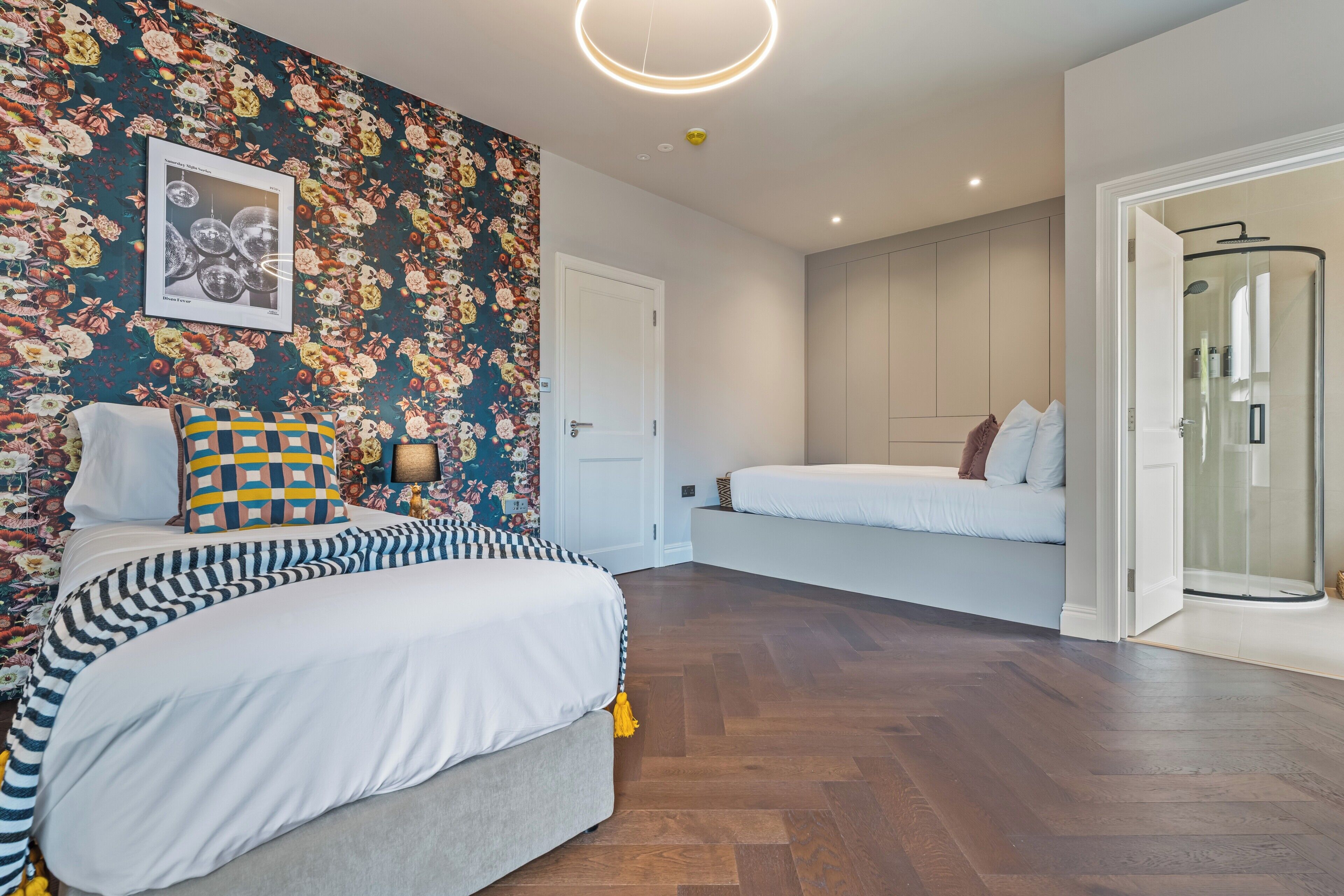 Ein modernes Schlafzimmer mit floralem Wandpapier, einem Bett mit gestreifter Bettwäsche, einem Nachttisch und einer Dusche.