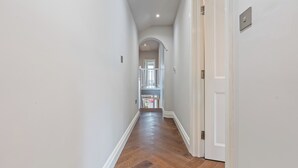 A hallway with a wooden floor, white walls, and a door on the right. - Luxury 8 Bed House, Games Room & Free Parking (Bedford)