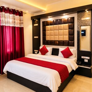 Quarto de hotel com uma cama grande, cabeceira com design acolchoado, mesa de cabeceira com telefone e televisão fixada na parede.