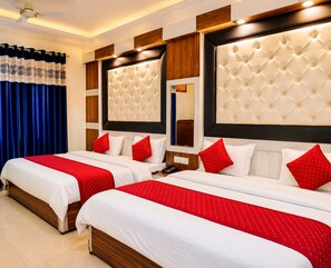 Quarto de hotel com duas camas, cada uma com cabeceira estofada, roupa de cama vermelha e branca, e piso de madeira.