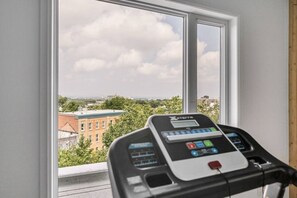 A treadmill with a digital display, positioned near a window overlooking a cityscape. - Cozy & Co | Le Spritz | Centre-ville + Parking (Québec City)